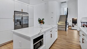 A modern kitchen with white cabinetry, a stainless steel refrigerator, a built-in oven, and a marble countertop. - NEW! Luxe Vacation Getaway - heated pool and putting green (Peoria)