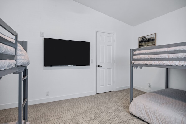 A room with bunk beds, a white door, a flat-screen TV, and a small painting on the wall.