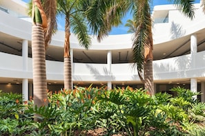 A multi-level atrium with palm trees and tropical plants, featuring a modern architectural design with white columns and a clear sky view.