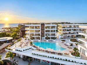 A resort with a central pool, multiple balconies, and a view of the ocean.