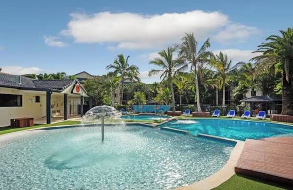 A swimming pool with a water fountain, surrounded by palm trees and lounge chairs. - The ultimate Family holiday at Turtle Beach Resort- Mermaid beach (Mermaid Beach)