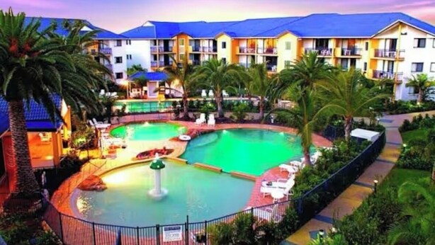 A hotel with a swimming pool, palm trees, and a blue-roofed building.