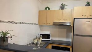 A compact kitchen with wooden cabinets, a stainless steel refrigerator, a microwave, and a dishwasher. There are two potted plants on the counter.