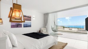 A modern bedroom with a large bed, a hanging chair, and a balcony with a city view. - The Blossom Villa by Elite Havens (Koh Samui)