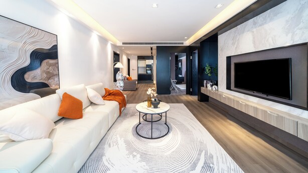 A modern living room with a white sofa, a round coffee table, and a flat-screen TV mounted on the wall.