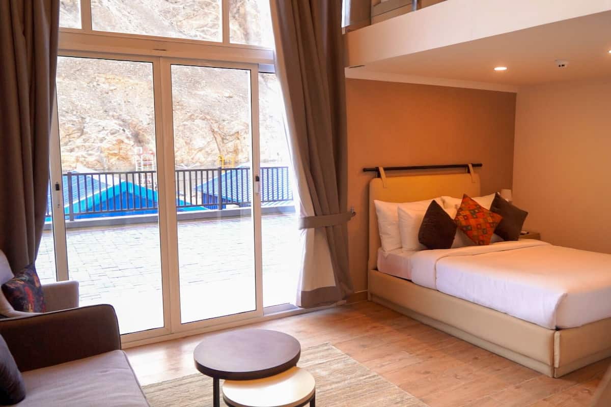 A hotel room with a bed, a small round table, and a view of a blue staircase outside.