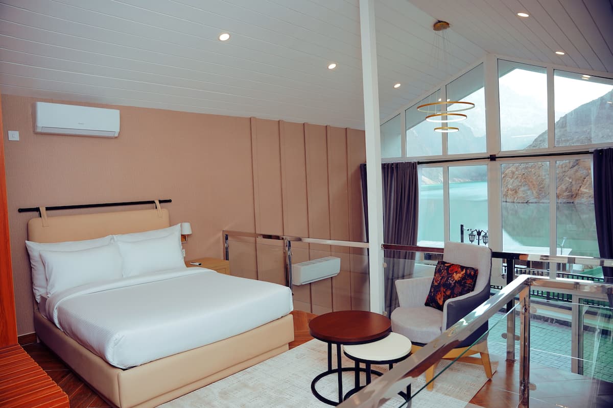 A modern hotel room with a large bed, a small table, a chair, and a balcony with a view of the mountains.