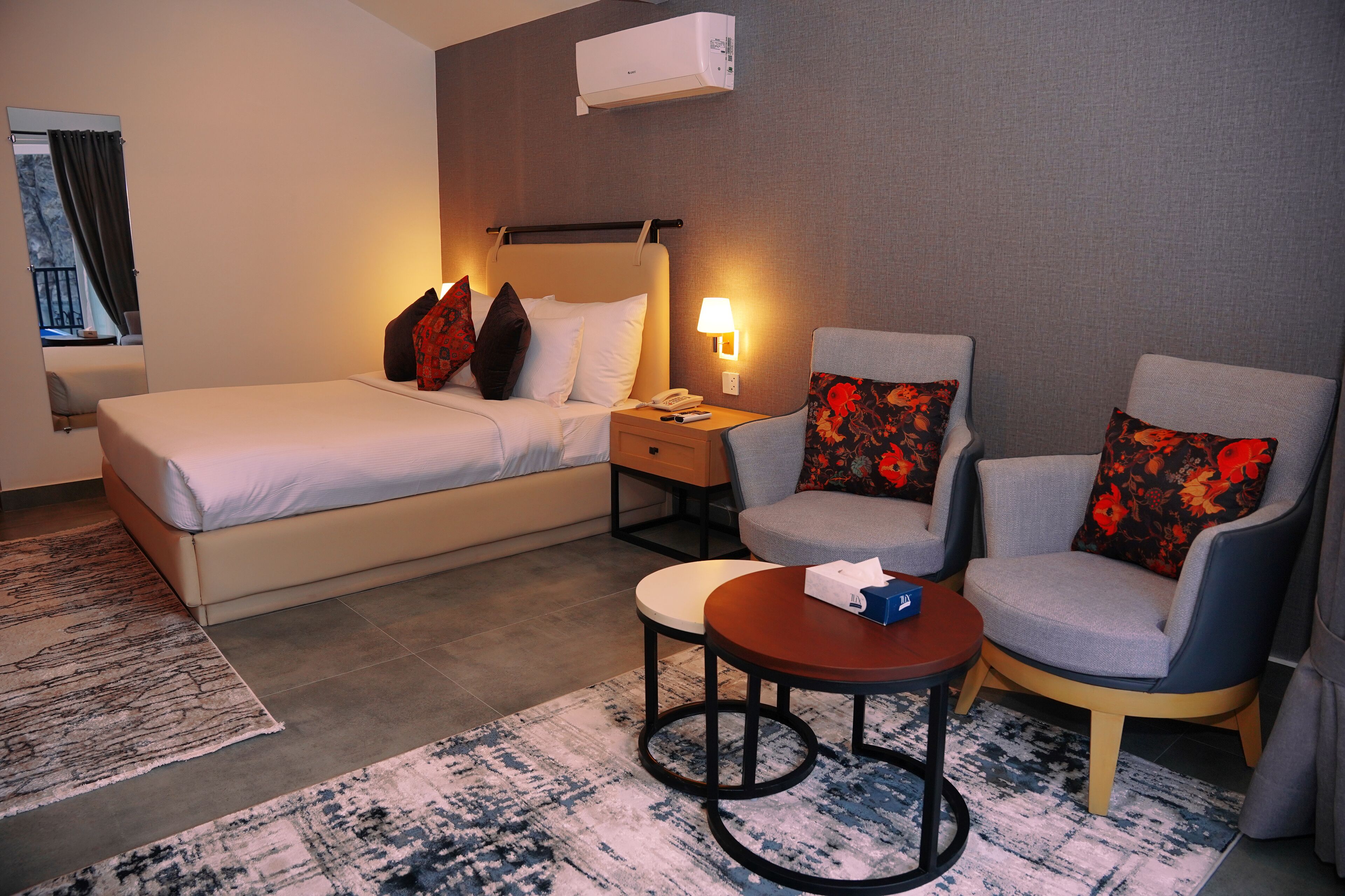 Habitación de hotel con cama, dos sillones, una mesita y una mesita de noche con lámpara.