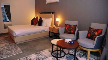 Habitación de hotel con cama, dos sillones, una mesita y una mesita de noche con lámpara.