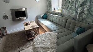 Una sala de estar moderna con un sofá gris, una mesa de centro de madera, un plaid blanco suave y un televisor montado en la pared.