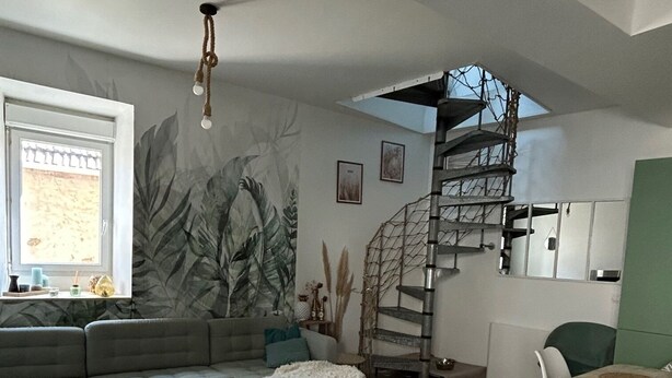 Un interior moderno con una escalera de caracol, un sofá, una zona de comedor y un mural en la pared.
