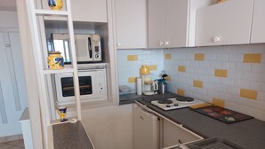A compact kitchen with white cabinets, a microwave, an oven, a gas stove, and a sink. - Location Banyuls-sur-Mer, Panoramic view (Banyuls sur mer)