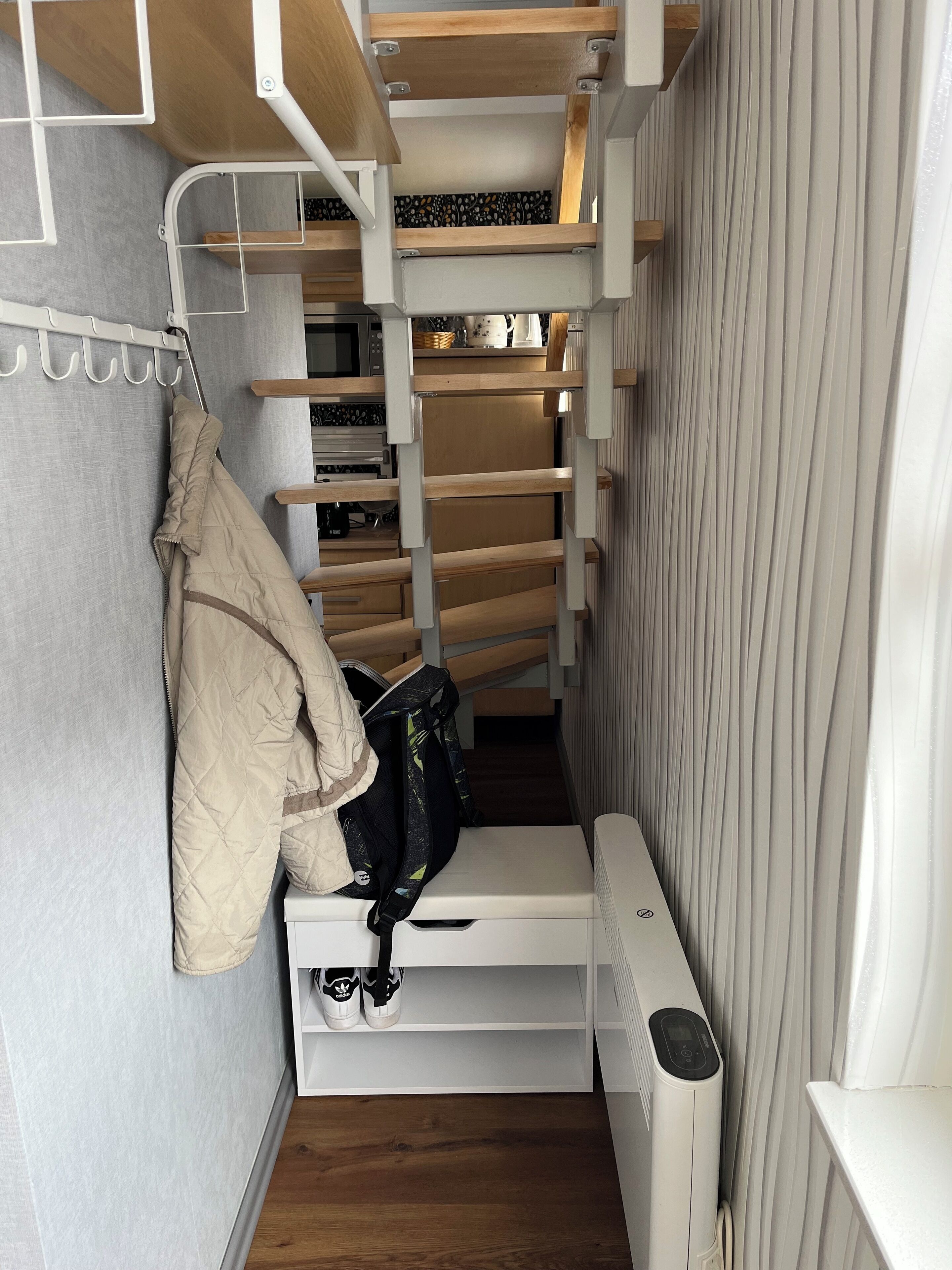 Habitación compacta y de varios niveles con estanterías y espacio de almacenamiento integrados, un radiador y un perchero.