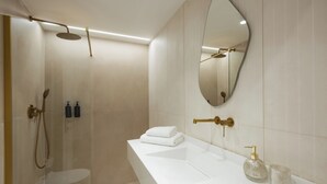 Un baño moderno con cabina de ducha de vidrio, lavamanos blanco con detalles dorados y un espejo grande.