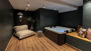 Un spa moderno con suelo de madera, una camilla de masaje, una bañera de hidromasaje y una planta pequeña.
