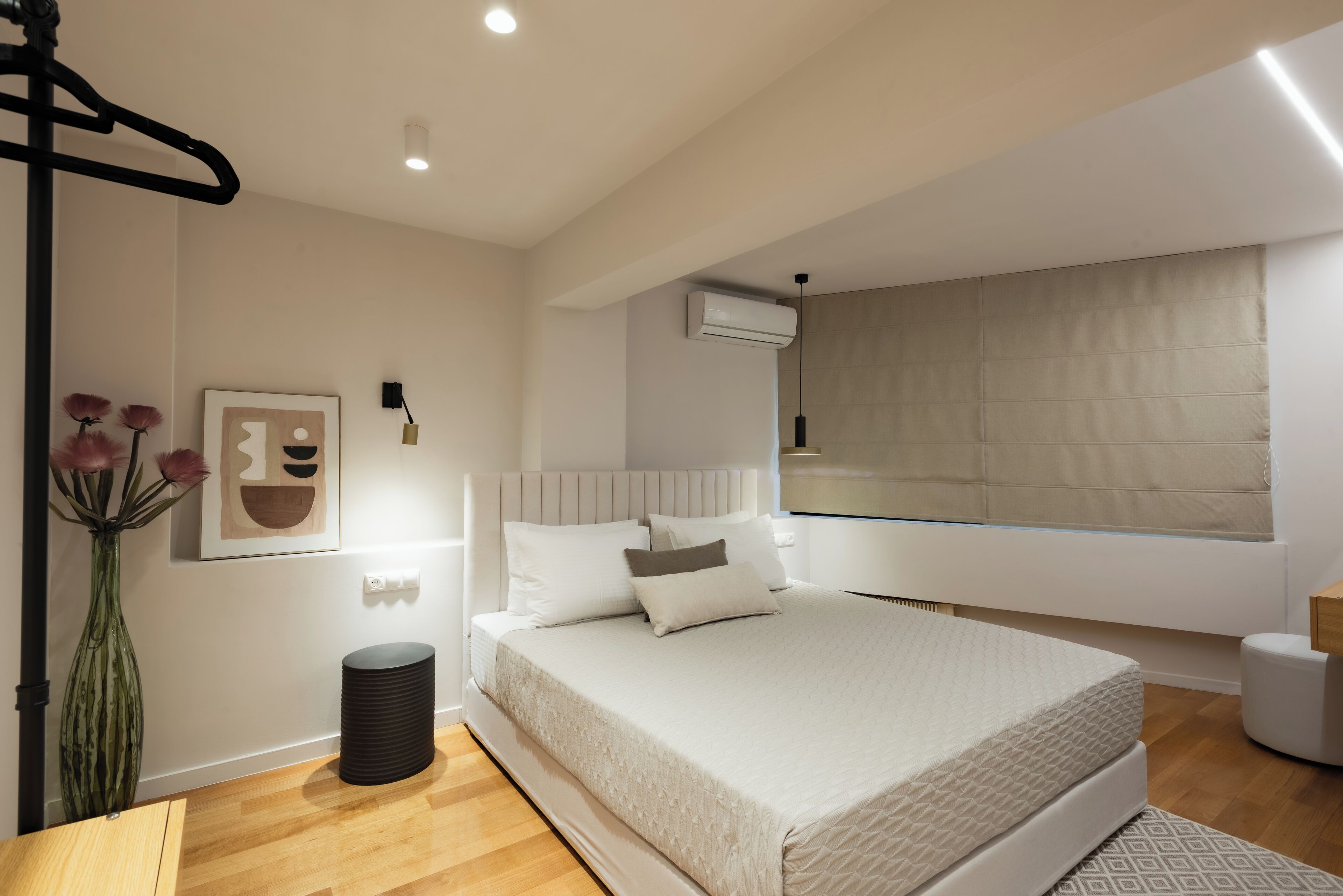 Une chambre à coucher moderne avec un grand lit, une table de chevet, un vase de fleurs et un climatiseur fixé au mur.
