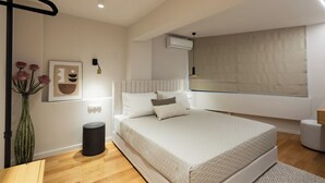 Un dormitorio moderno con una cama grande, una mesita de noche, un jarrón con flores y un aire acondicionado instalado en la pared.