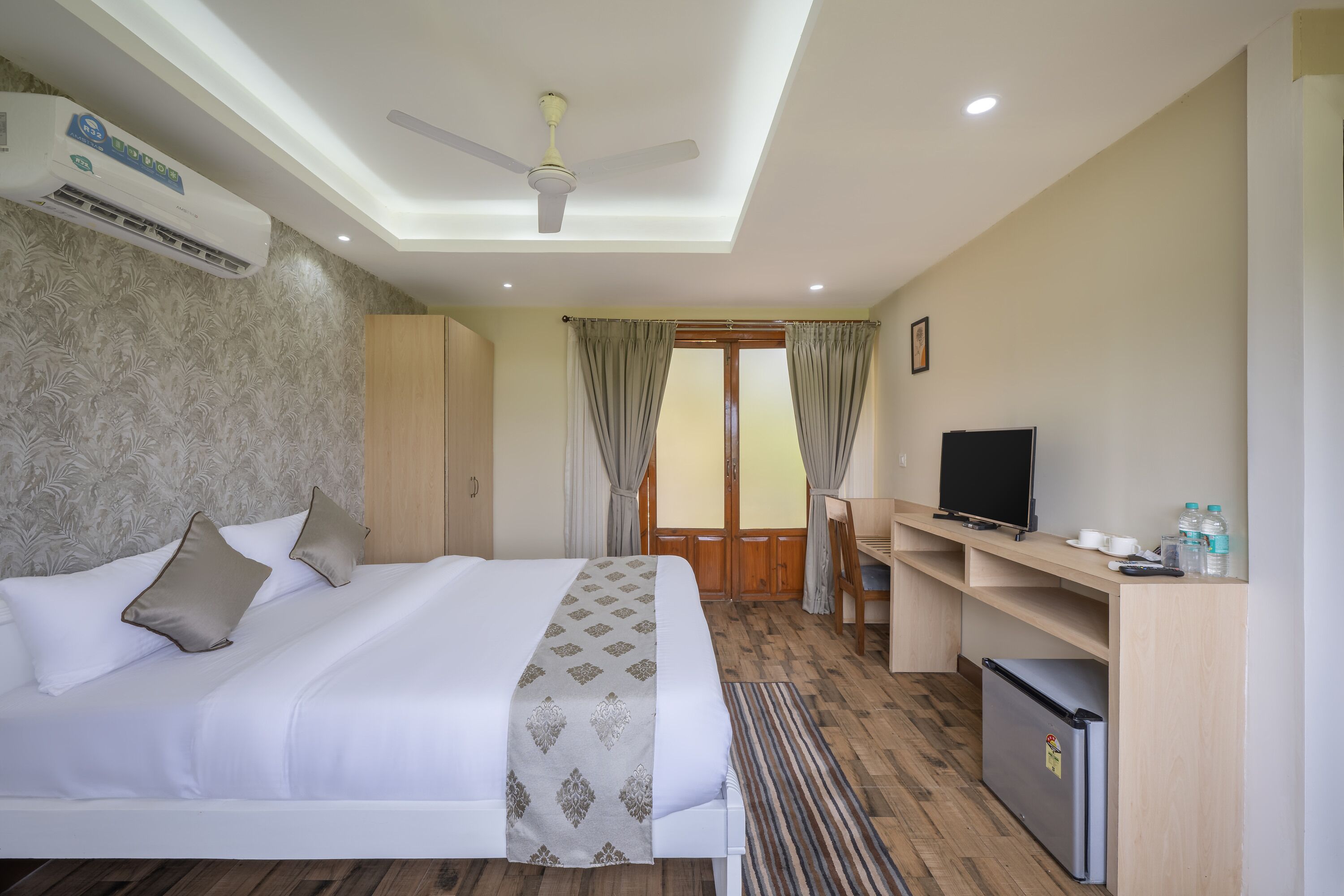 A hotel room with a bed, a desk, a television, and a refrigerator.
