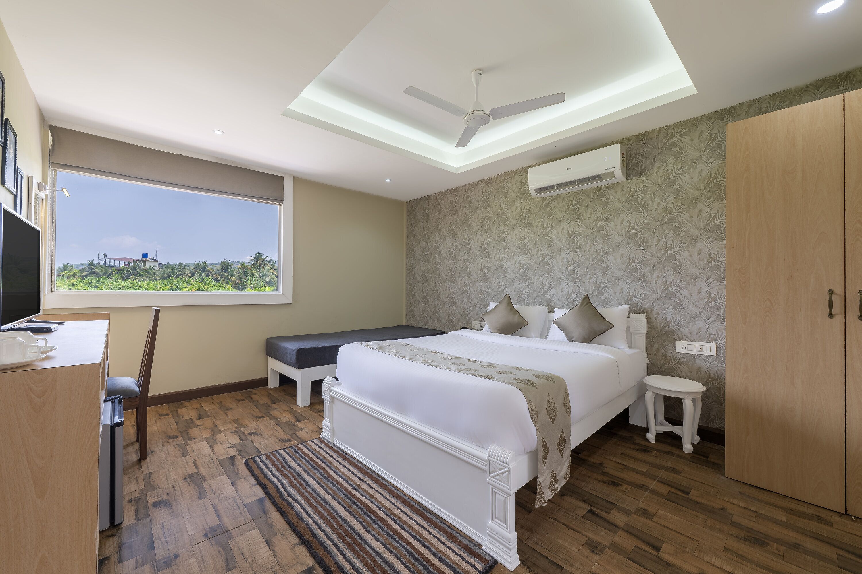 A bedroom with a bed, bedside tables, a desk, a chair, a ceiling fan, and a window with a view.
