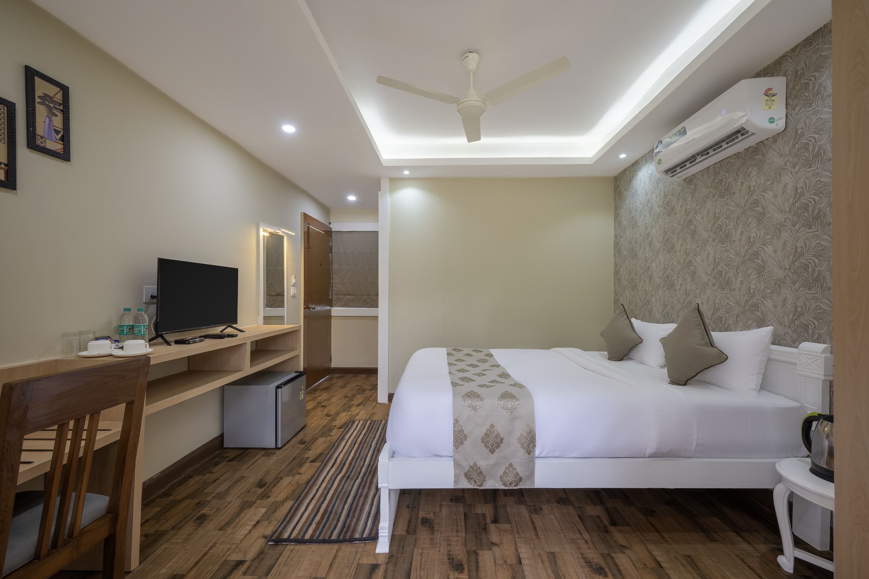 A hotel room with a bed, desk, chair, television, and an air conditioning unit.