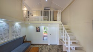 Una habitación con zona de descanso en altura, sofá, banca y escalera.