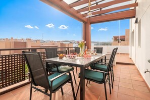 Un balcón con mesa lista para comer, sillas, un florero con flores y vista a la ciudad.