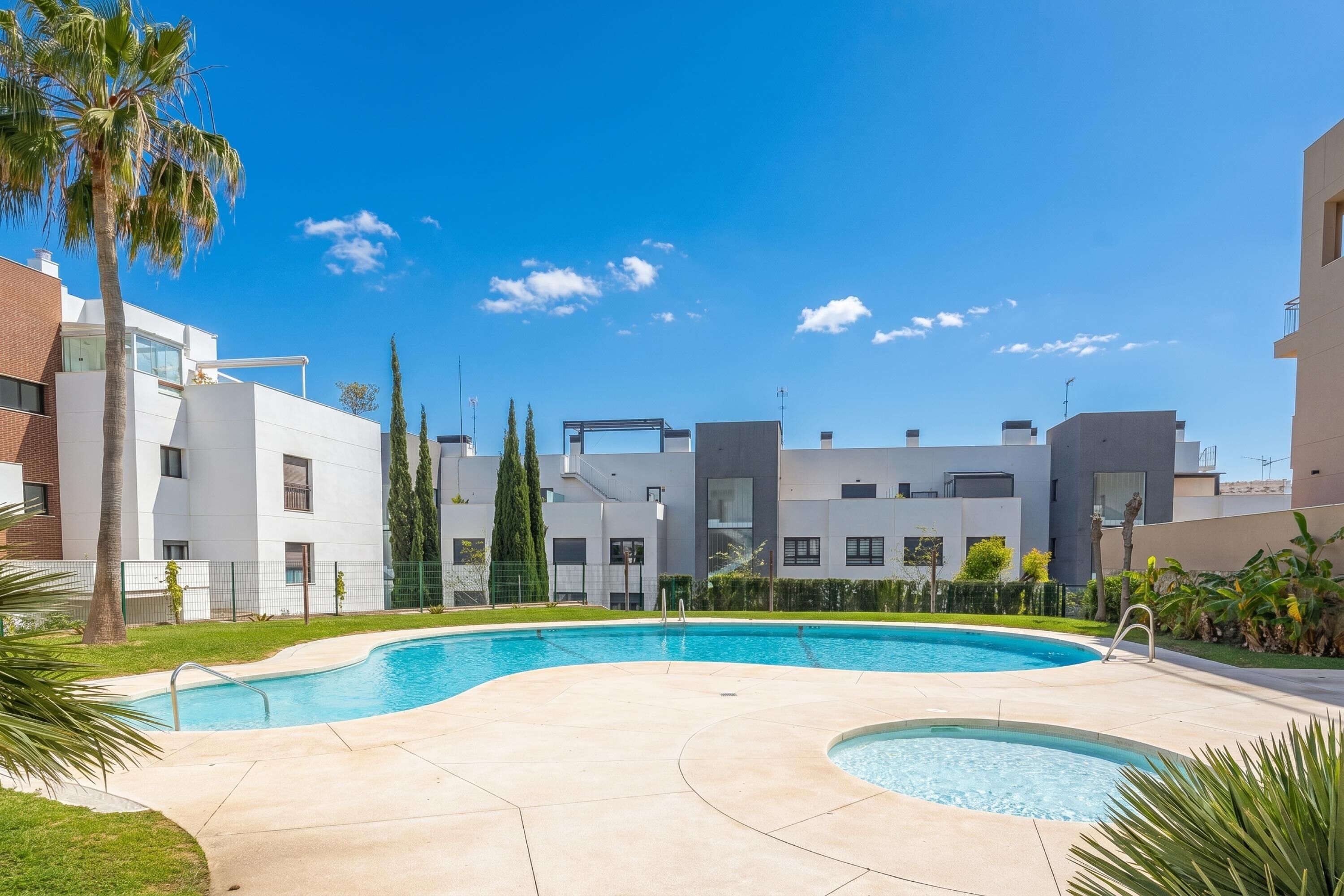 Un immeuble résidentiel moderne doté d’une piscine, entouré de verdure et de palmiers.