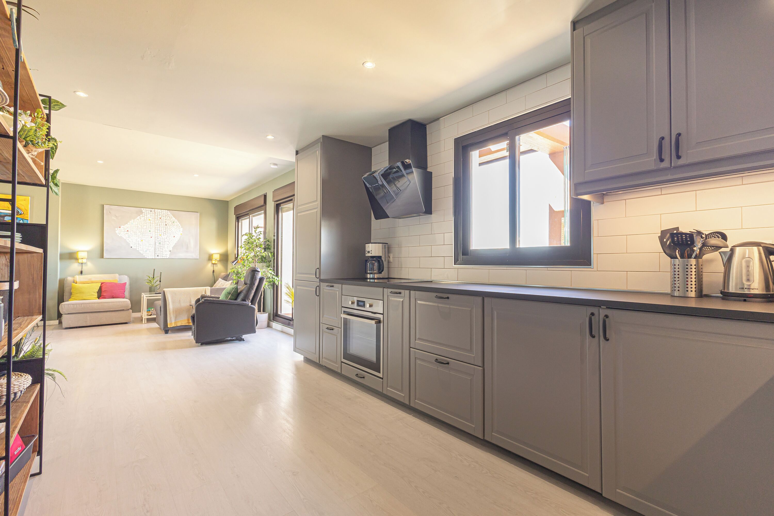 A modern kitchen with grey cabinets, a built-in oven, and a window above the counter.