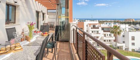 Un balcón con mesa y sillas dispuestas, y vistas al mar y edificios.