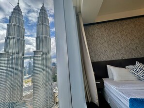 Una habitación de hotel con cama, mesita de noche y vistas a las Torres Petronas.