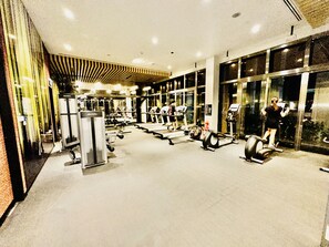Un gimnasio con diverso equipo de ejercicio, incluyendo cintas de correr y máquinas de pesas, y un amplio ventanal en un lateral.