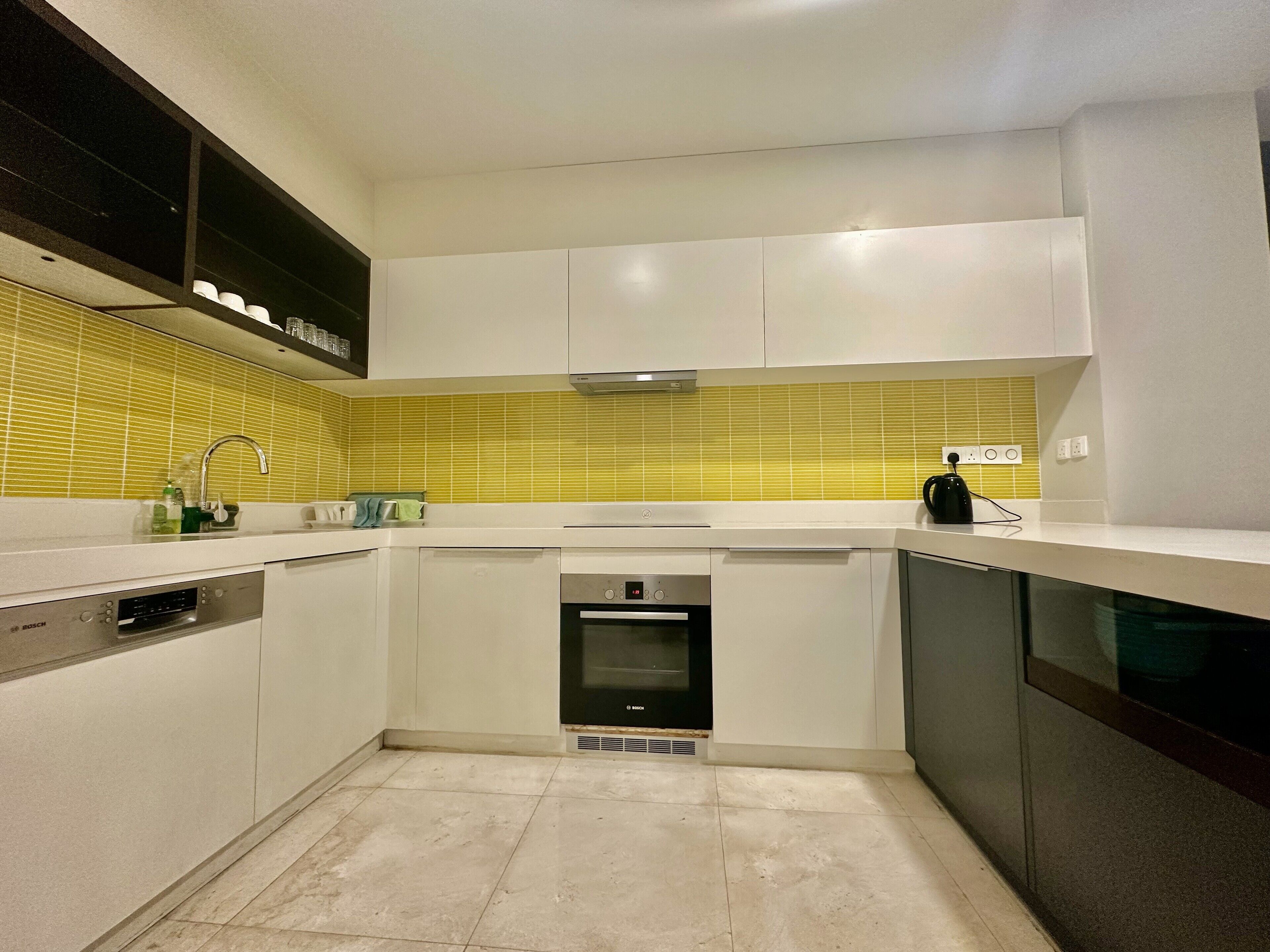 Una cocina moderna con armarios blancos, lavavajillas Bosch, horno y salpicadero de azulejos amarillos.