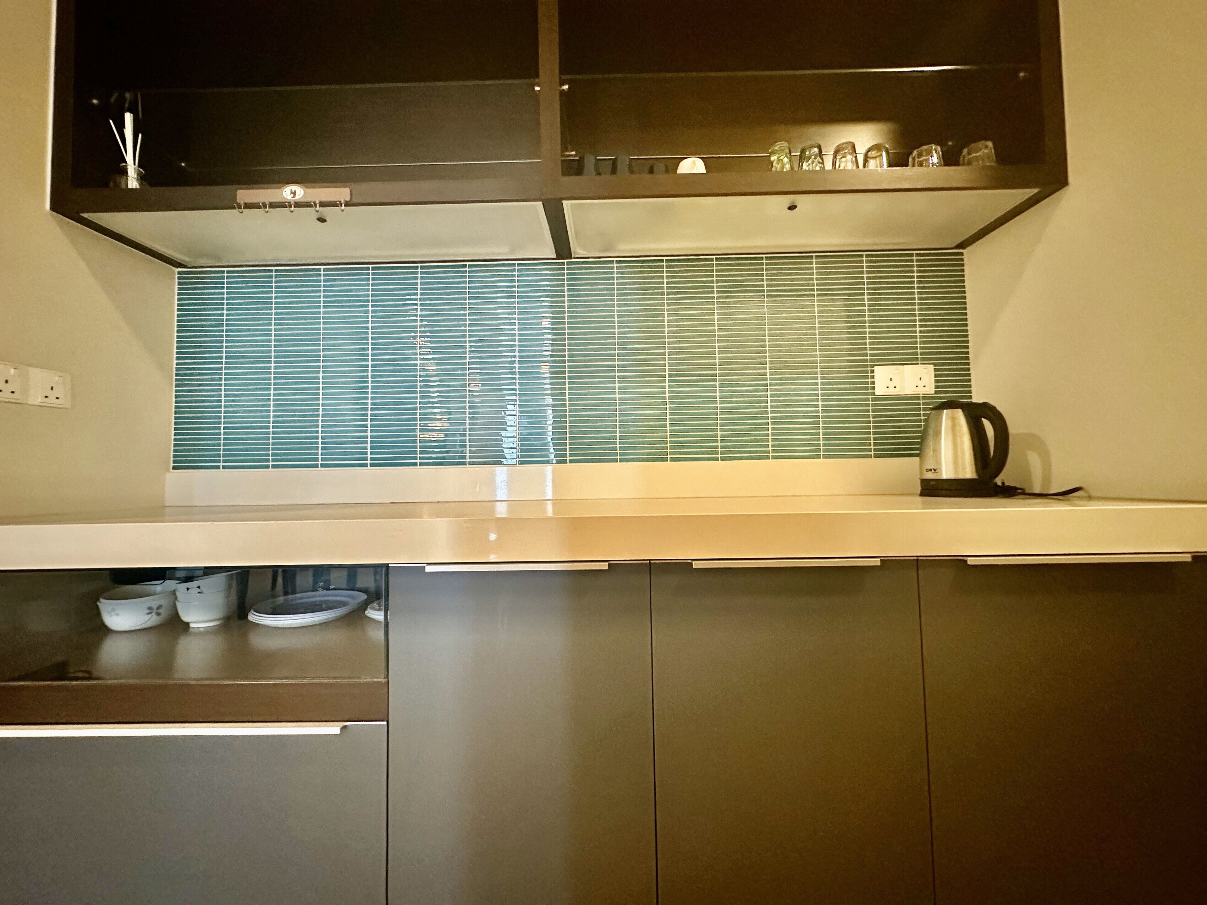 A modern kitchen with a stainless steel range hood, a backsplash with blue tiles, and a kettle on the counter.