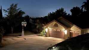 Un camino de entrada residencial que lleva a un garaje con iluminación decorativa y un aro de baloncesto.