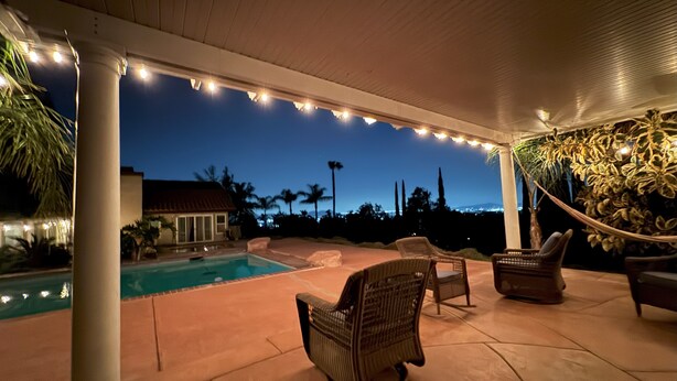 Un espacio al aire libre cubierto con piscina, sillas de mimbre y luces colgantes.