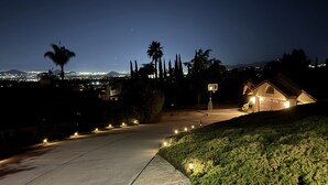 Una entrada residencial de noche con un aro de baloncesto, un garaje y un camino bien iluminado.