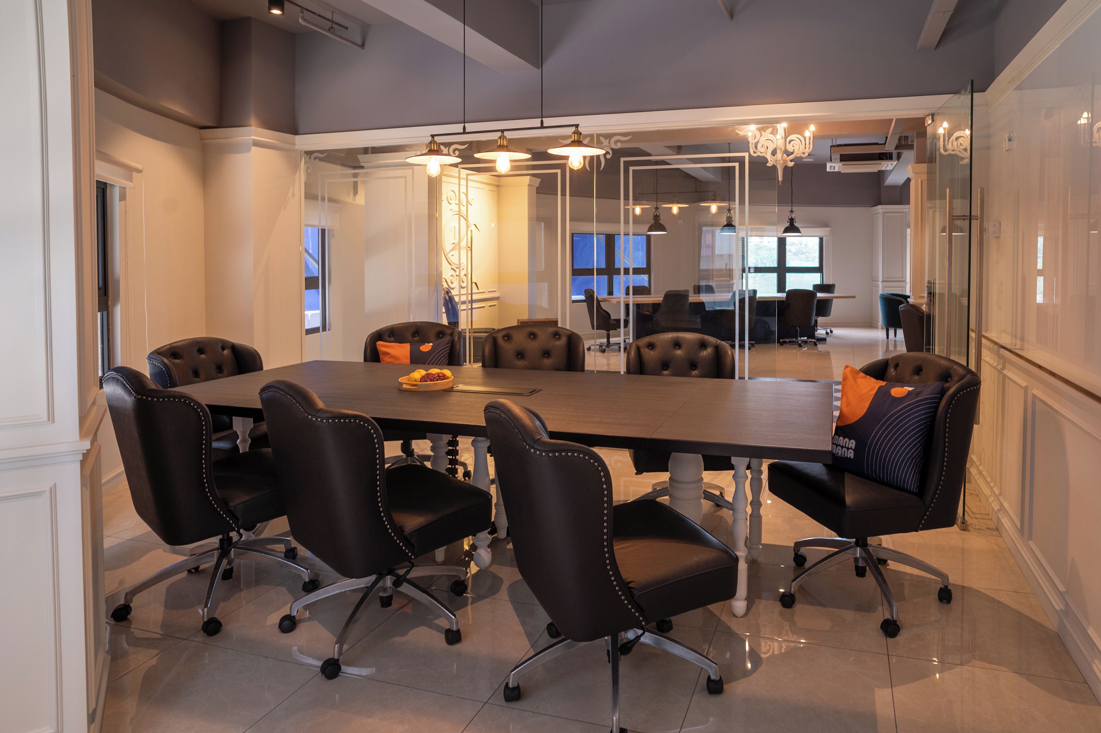 A conference room with a long table, six black leather chairs, and a glass partition.