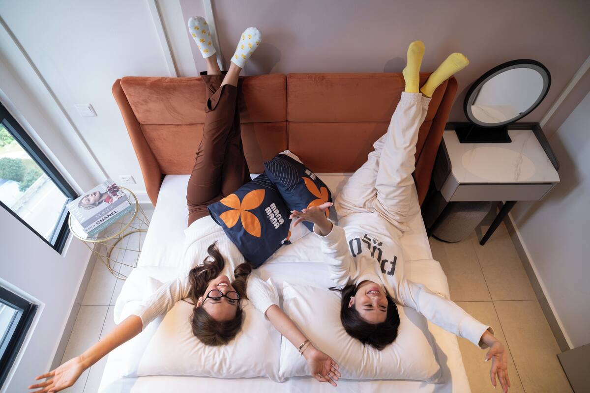 A bed with two people lying on it, a bedside table with a magazine, and a small mirror on a stand.