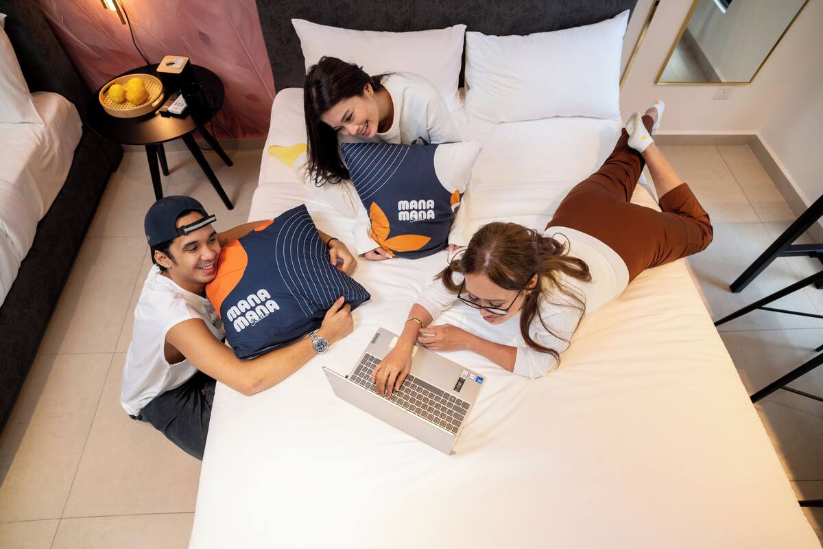 A bedroom with a bed, a laptop, and three people lying on the bed.