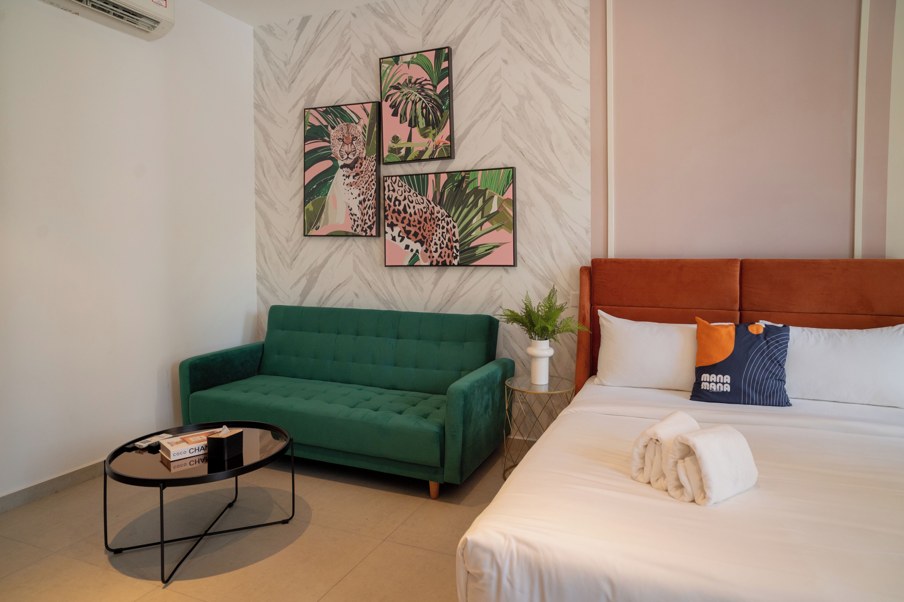Een hotelkamer met een groene bank, een bed met wit bedlinnen, en drie ingelijste foto’s aan de muur.