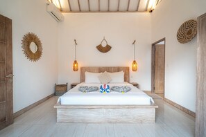 A spacious bedroom with a large bed, wooden headboard, and two wall-mounted pendant lights. - Villa Kayu (Gili Air)