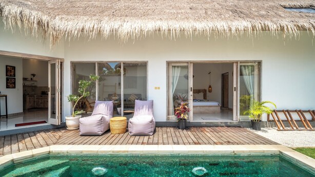 Una villa moderna con techo de paja, piscina y patio con mobiliario.