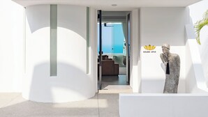 Ein modernes Gebäude mit weißer Fassade und einer Glastür, die zu einem Raum mit Meerblick f ührt. Eine goldene Lotusstatue ist auf der rechten Seite sichtbar.