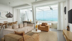 Ein geräumiges Wohnzimmer mit einer großen Eckcouch, einem runden Couchtisch und Blick aufs Meer.