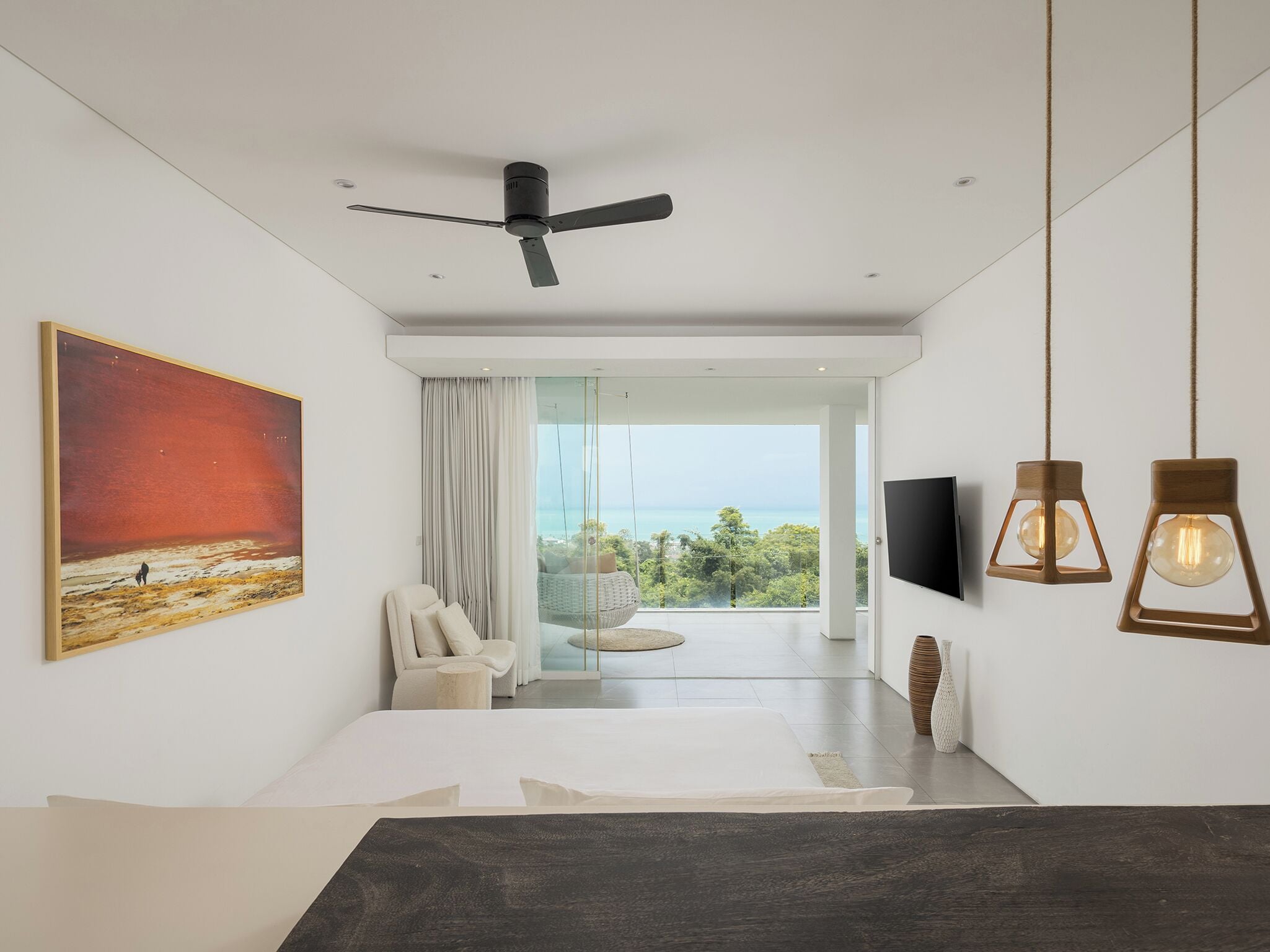 Ein modernes Schlafzimmer mit großem Fenster, Deckenventilator, Gemälde und Fernseher an der Wand.