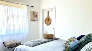 Une chambre à coucher avec un lit, des oreillers, une chaise, une porte et un panier.