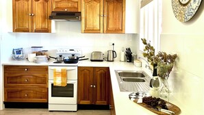 Une cuisine avec des meubles de rangement en bois, une cuisinière, un évier et une horloge au mur.