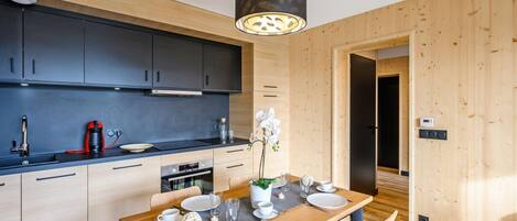Une cuisine moderne avec des meubles de couleur sombre, une table à manger en bois pour quatre personnes et un luminaire suspendu au-dessus.