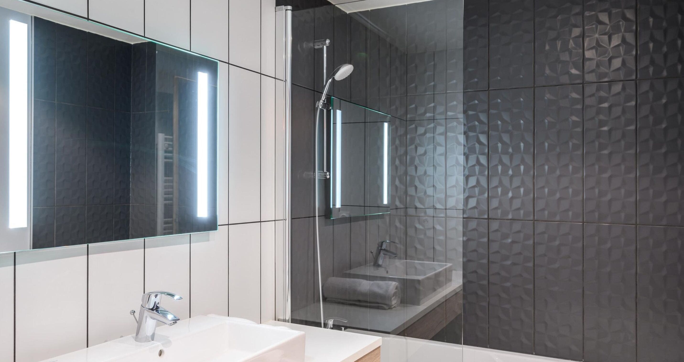 Un bany modern amb un mirall gran, un lavabo blanc i una zona de dutxa.