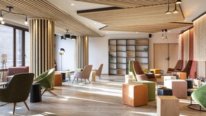 Un espace de détente moderne avec un plancher en bois, de nombreux sièges, dont des fauteuils et des poufs aux couleurs vives, et une grande bibliothèque.